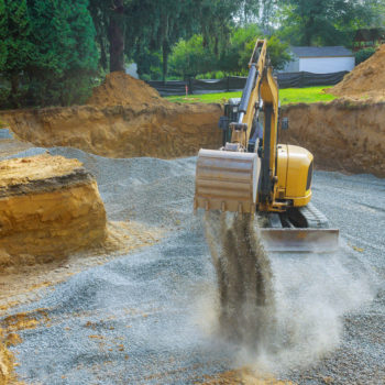 Excavator digging bucket scooping gravel from a building foundation